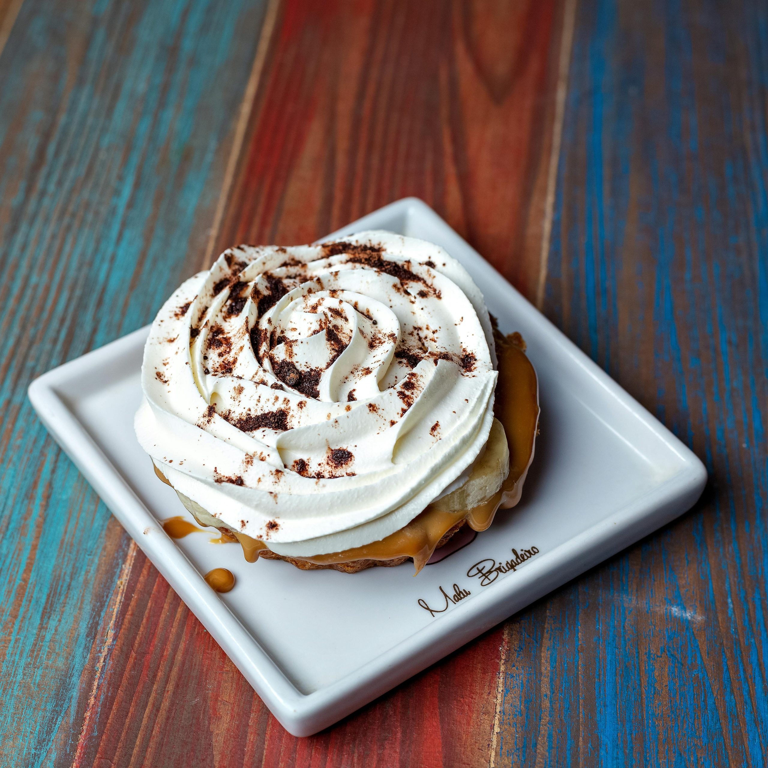 Close-up of a creamy banoffee pie with caramel and frosting on a ceramic plate.
