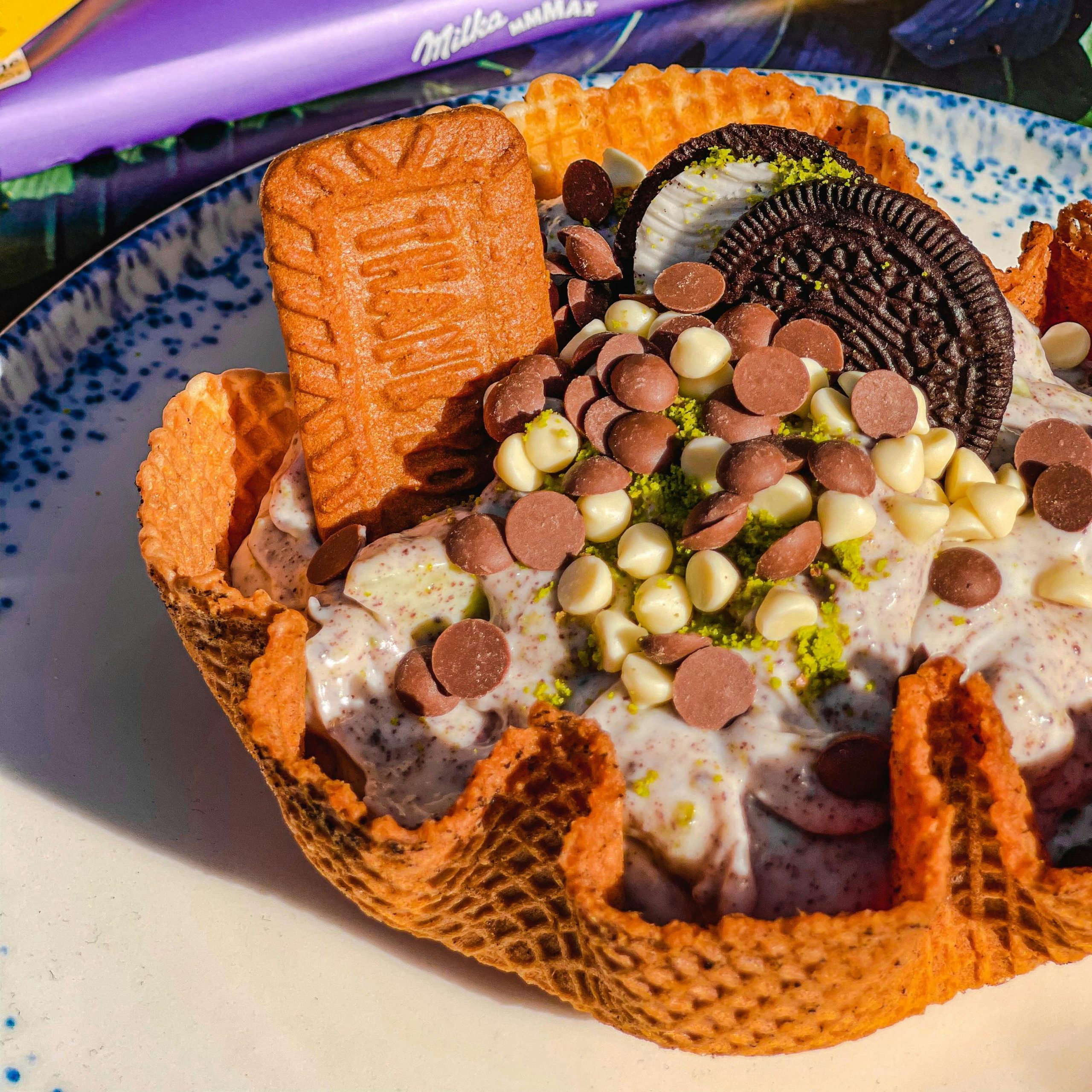 Indulgent ice cream sundae with cookies and chocolates in a waffle bowl.